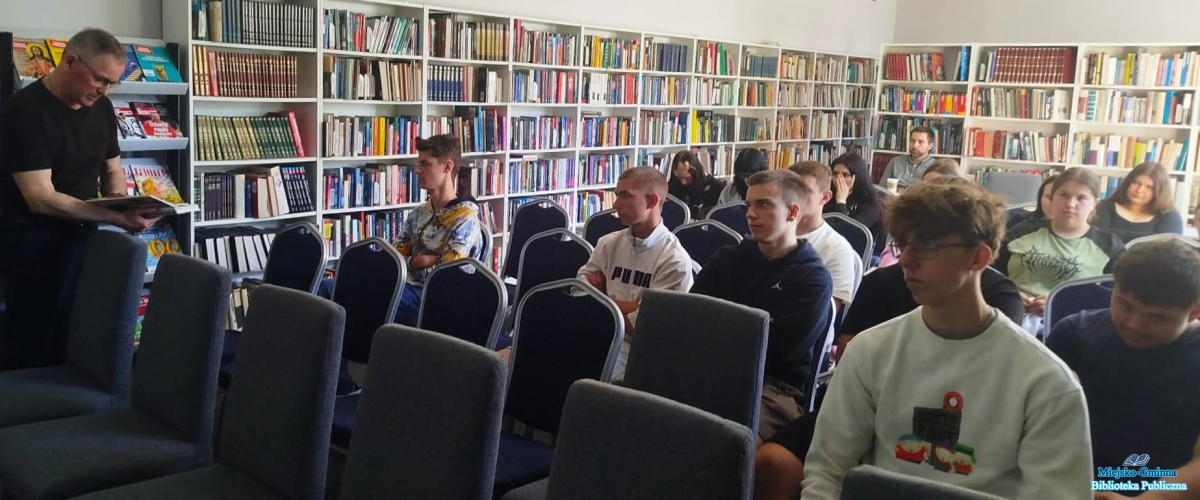 Młodzież siedzi, a Pan stoi obok i trzyma książkę Młodzież siedzi, a Pan stoi obok i trzyma książkę