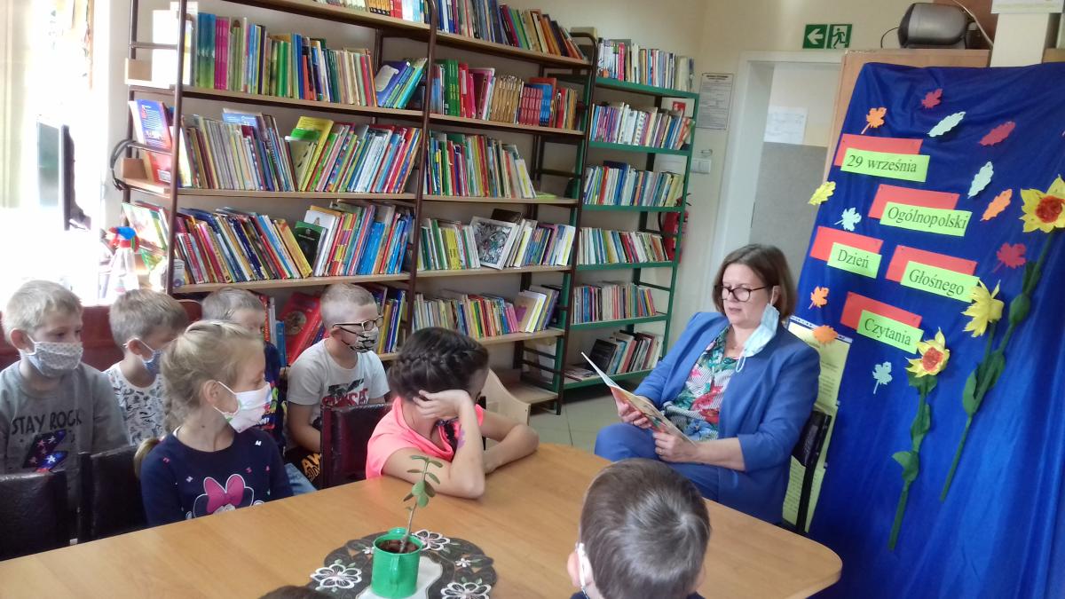 Pani w bibliotece czyta książkę dla siedmiorga dzieci.