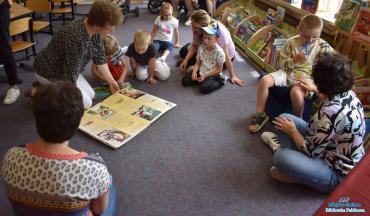 Dzieci siedzą na dywanie oglądają książkę