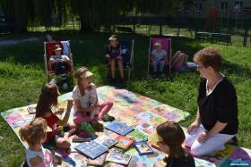 Bibliotekarka podczas rozmowy z dziećmi siedzącymi na matach wśród leżących książek